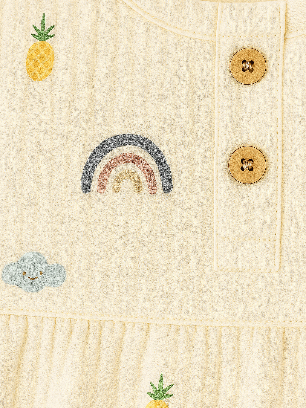 Beige fabric with embroidered elements including a rainbow, cloud, and pineapple on a buttoned surface.